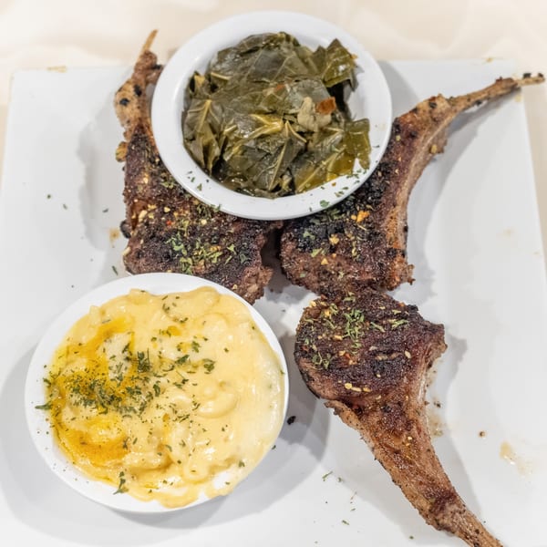 Grilled lamb chops with sides of mac and cheese and collard greens on a white plate.