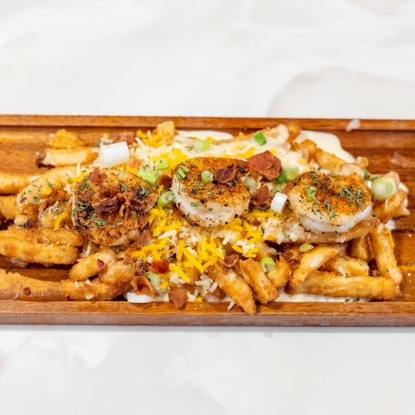 Shrimp and fries topped with cheese, bacon bits, and green onions on a wooden board.