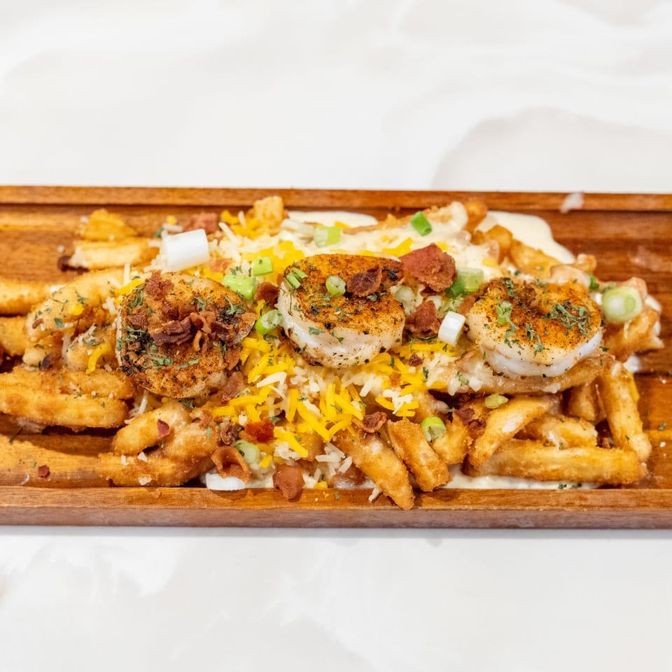 Shrimp and fries topped with cheese, bacon bits, and green onions on a wooden board.