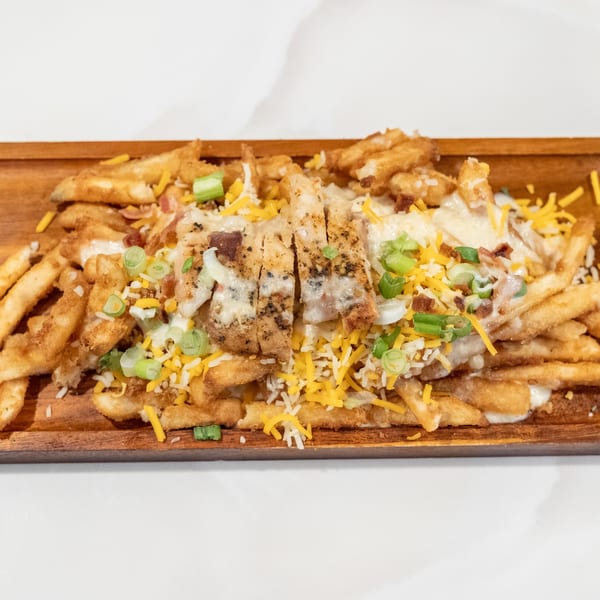 Fries topped with grilled chicken, melted cheese, bacon bits, and green onions on a wooden board.